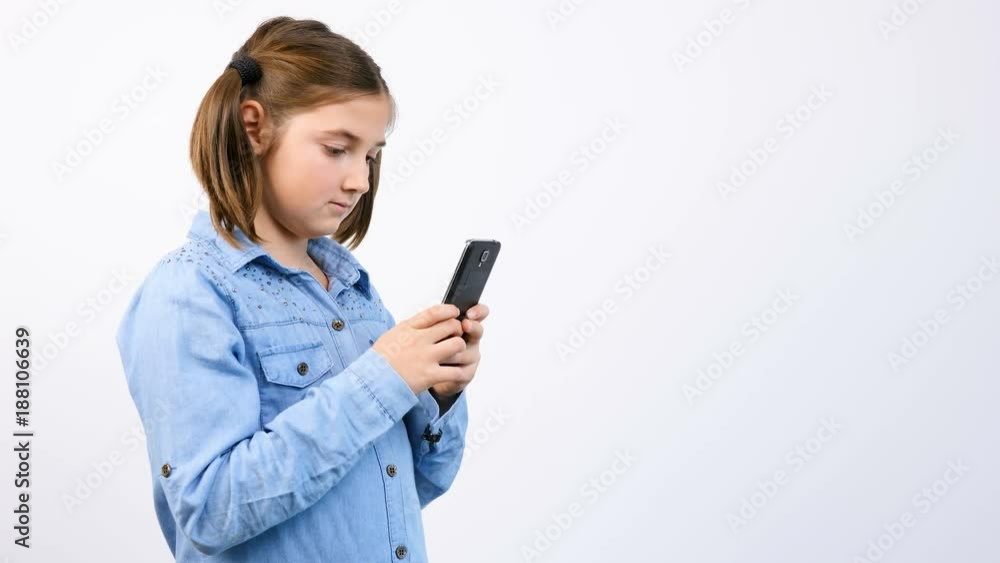 Toung pretty girl child using smartphone on gray background in studio Toung pretty girl child using smartphone on gray background in studio
