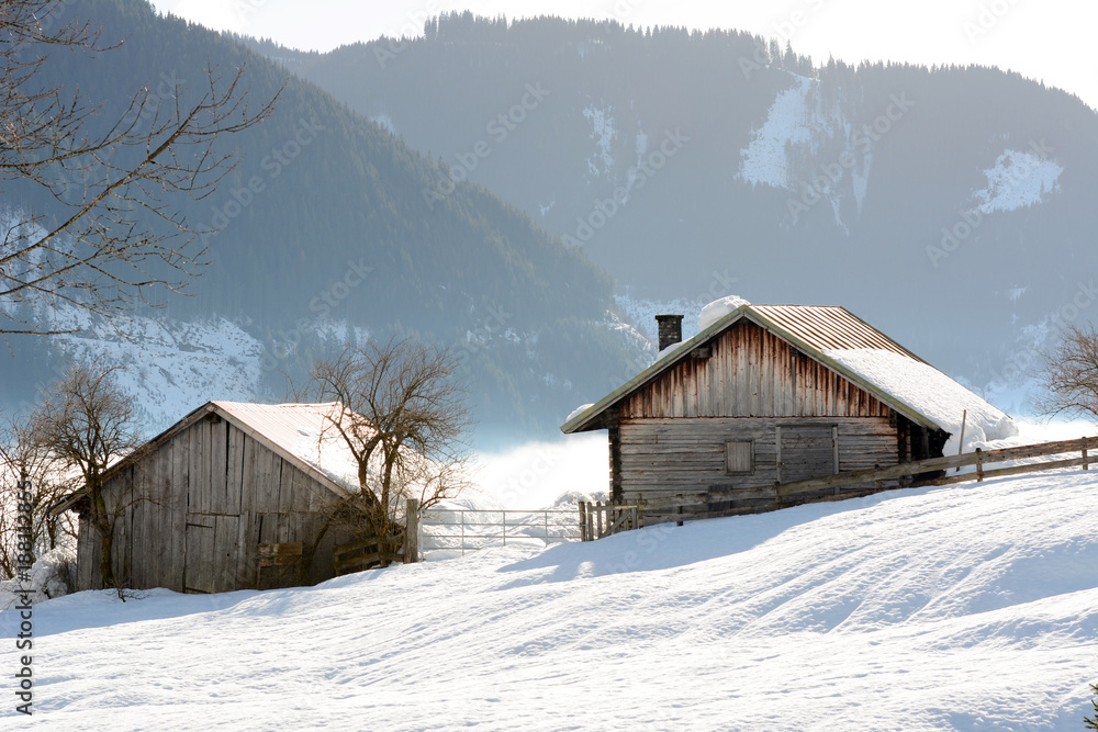 Winter landscape at early morning in Austria with snow, wooden buildings, blue sky and copy space.