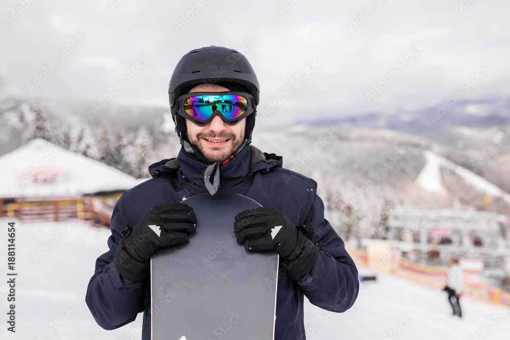 Man snowboarder stands with snowboard. Closeup portrait.