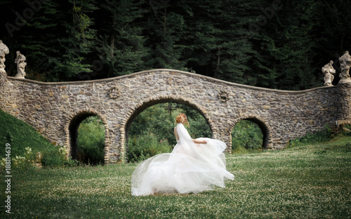 The bride in a beautiful dress dances the waltz near the stone bridge in the park