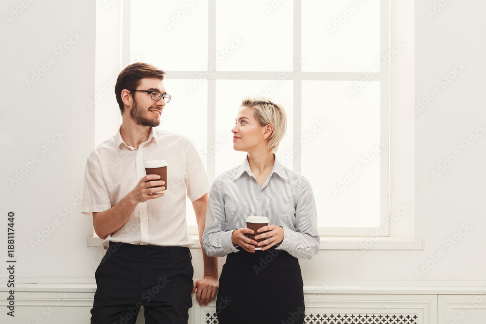 Fototapeta premium Couple of young colleagues drink coffee near window