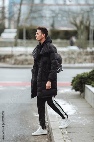 Stylish man wolk on the street. Winter cold outfit. Big jacket with white sneakers. Blured background street. Profecional model photo. photo