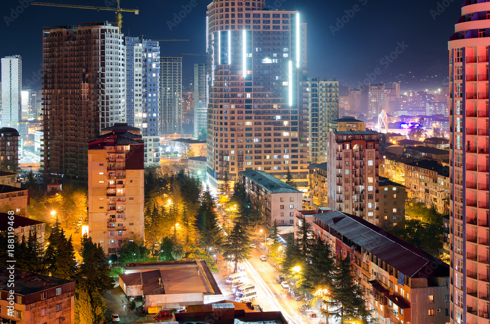 View of the streets of the night city of Batumi with skyscrapers, light from the windows of apartment buildings, traffic of cars on the road. Urban life.