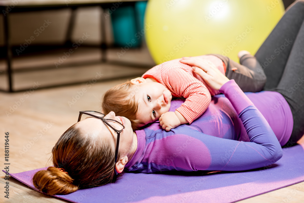 Portrait of a young mother in sportswear lying with her baby boy relaxing after the exercise at home Portrait of a young mother in sportswear lying with her baby boy relaxing after the exercise at home