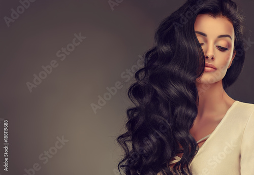 Brunette girl with long and shiny wavy hair . Beautiful model woman with curly hairstyle . 