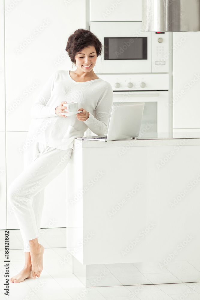 Portrait of a young pretty woman with long black curly hair at home kitchen with laptop on background at morning Portrait of a young pretty woman with long black curly hair at home kitchen with laptop on background at morning
