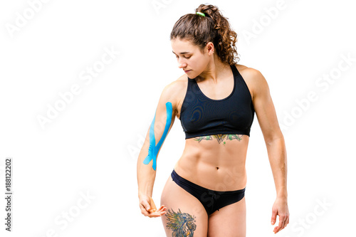 Concept of sports medicine and health. A young cowish girl with a good figure posing on a white isolated background with a kinesiology tape, a sticky blue ribbon on her arm. Alternative medicine photo