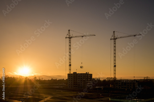 Silhouette tower cranes and unfinished multi-storey high buildings under construction at the sunset in desert on illuminated building site © hiv360