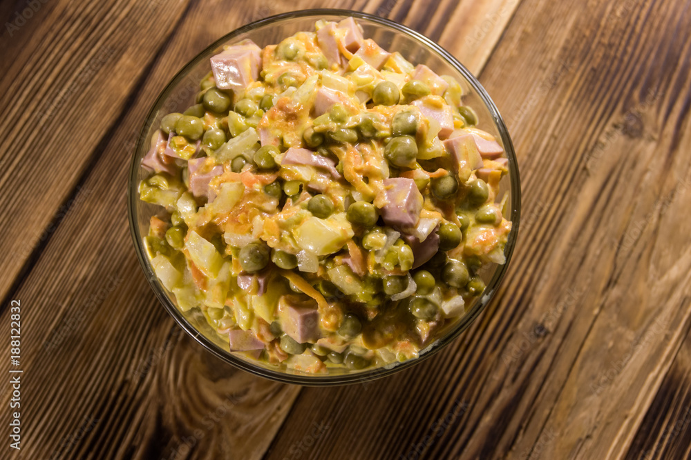 Mayonnaise salad with sausage, green pea, carrot and onion on wooden table