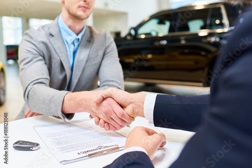 Close up of handsome client shaking hands with sales manager after signing purchase contract to buy new car in showroom