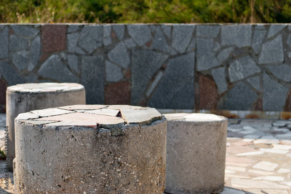 Composition of three low concrete stone pillars, against a background of a large stone tile texture, mosaic, bright summer sunny day, fence stone fence Composition of three low concrete stone pillars, against a background of a large stone tile texture, mosaic, bright summer sunny day, fence stone fence