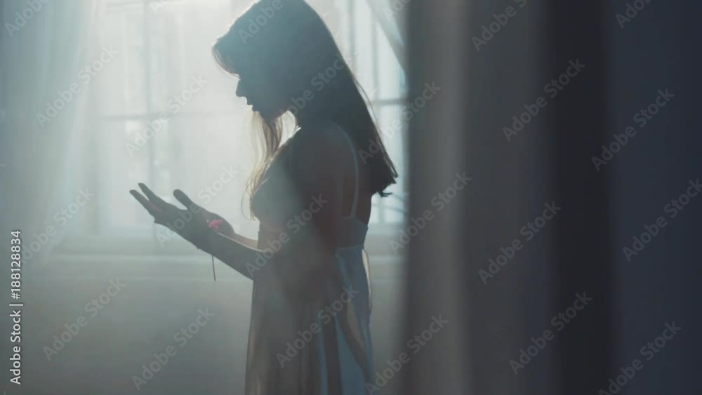 insane woman in a white nighty stands alone in the dark room and ...
