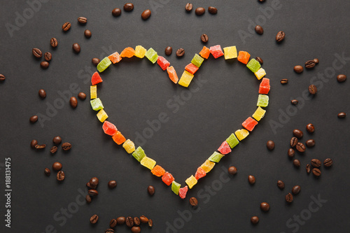 Colorful candied fruits in the form of heart with brown coffee beans isolated on black background for design. Saint Valentine's Day card on fabruary 14, holiday concept. Copy space for advertisement.