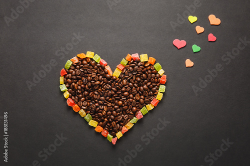 Colorful paper, candied fruits in the form of heart, brown coffee beans isolated on black background for design. Saint Valentine's Day card, fabruary 14, holiday concept. Copy space for advertisement.