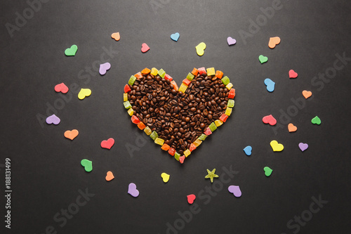 Colorful paper, candied fruits in the form of heart, brown coffee beans isolated on black background for design. Saint Valentine's Day card, fabruary 14, holiday concept. Copy space for advertisement.