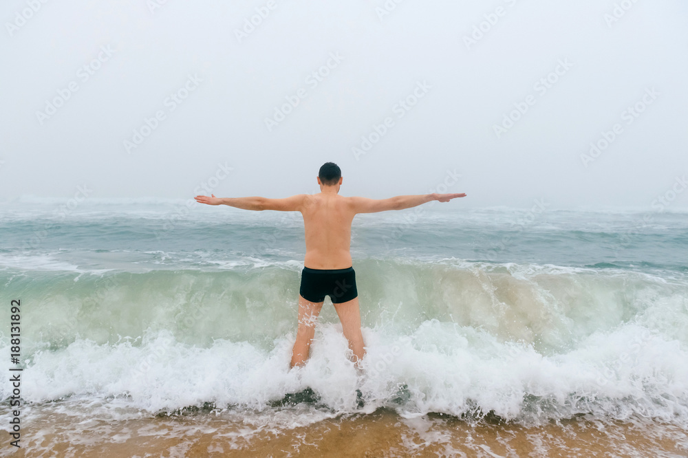 Odd bizarre crazy fearless awesome adult man enjoying in cold stormy sea. Guy jumping in waves in ocean with emotional funny face. Adult male fooling like child in water outdoors. Leisure activities Odd bizarre crazy fearless awesome adult man enjoying in cold stormy sea. Guy jumping in waves in ocean with emotional funny face. Adult male fooling like child in water outdoors. Leisure activities