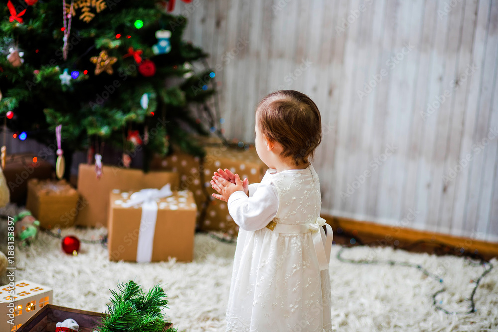 A cute little baby poses near a Christmas tree A cute little baby poses near a Christmas tree