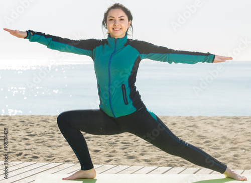 woman doing yoga poses on sunny beach by ocean