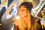 Portrait of young beautiful woman with sparkler in front of Christmas decoration outdoors