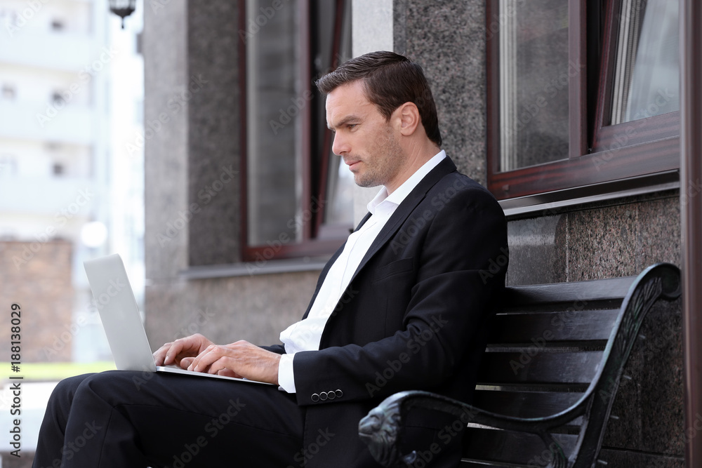 Fototapeta premium Man sitting on bench outdoors and using laptop