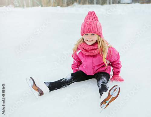 Little smiling girl skate and fell on ice in pink wear. Outdoor. photo