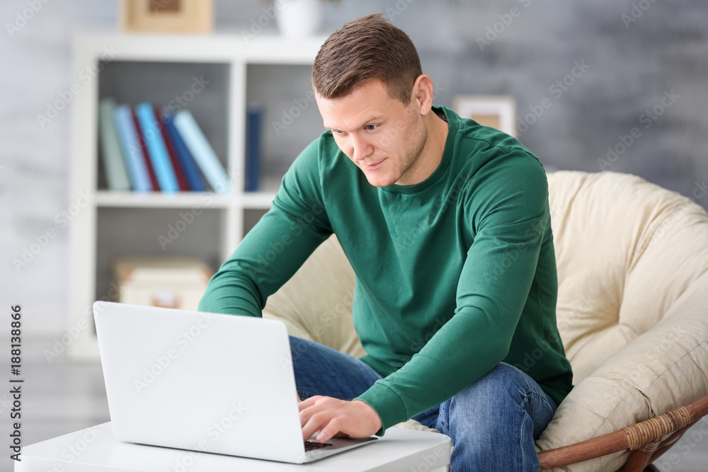 Young man using laptop on armchair indoors Young man using laptop on armchair indoors