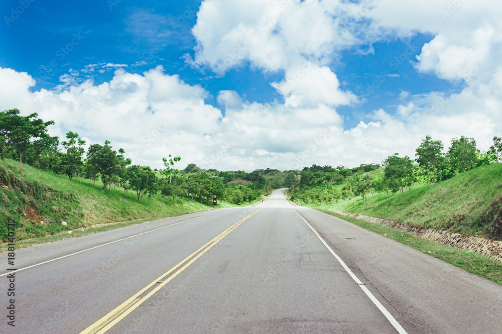 Road crossing the forest with cloudy sky and mountain view.