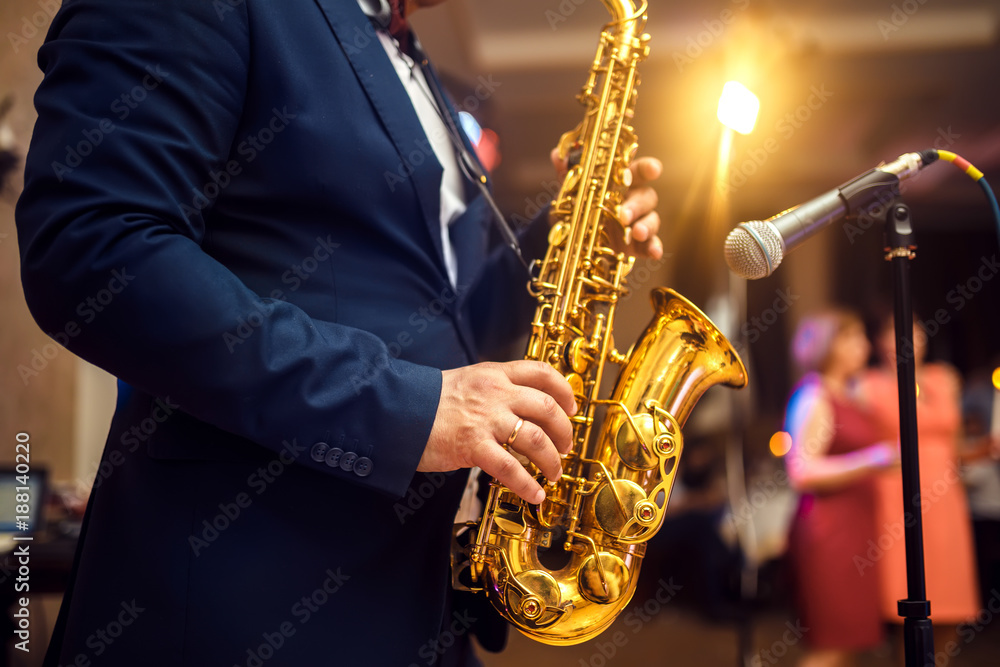 Obraz premium young musician man plays tenor saxophone on stage with light bokeh effected over blurred music instrument background 