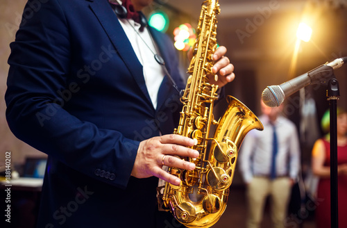 young musician man plays tenor saxophone on stage with light bokeh effected over blurred music instrument background 