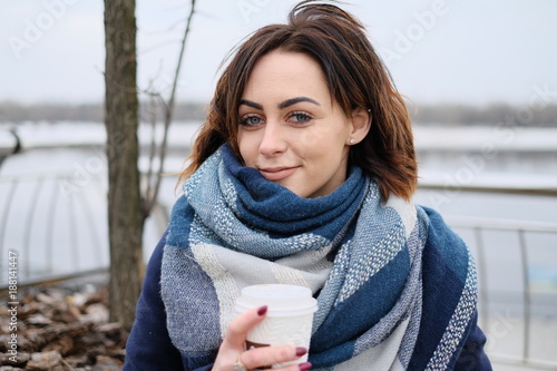 Portrait of attractive young woman wearing scarf and holding white coffee cup on a cold and snowy winter day