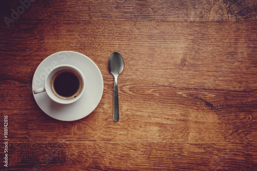 top view of white Cup with black coffee on a white saucer and teaspoon on dark brown wooden background