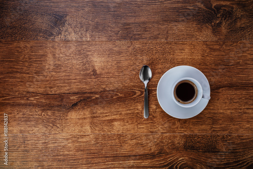 top view of white Cup with black coffee on a white saucer and teaspoon on dark brown wooden background