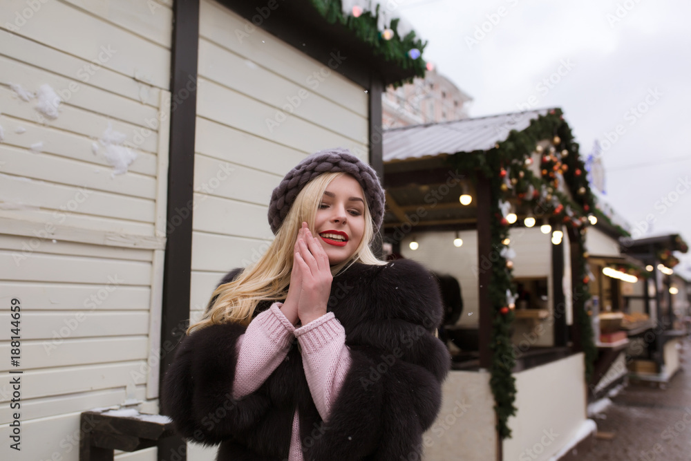 Street portrait of elegant young woman wearing stylish knitted hat and fur coat, posing at the Christmas fair. Empty space Street portrait of elegant young woman wearing stylish knitted hat and fur coat, posing at the Christmas fair. Empty space
