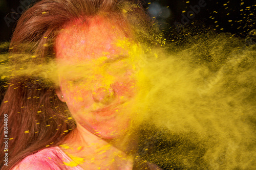 Closeup portrait of amazing brunette girl with Holi paint blowing into her face