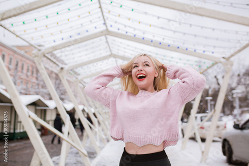 Cool blonde woman with bright makeup  wearing pink sweater  posing at the street in winter