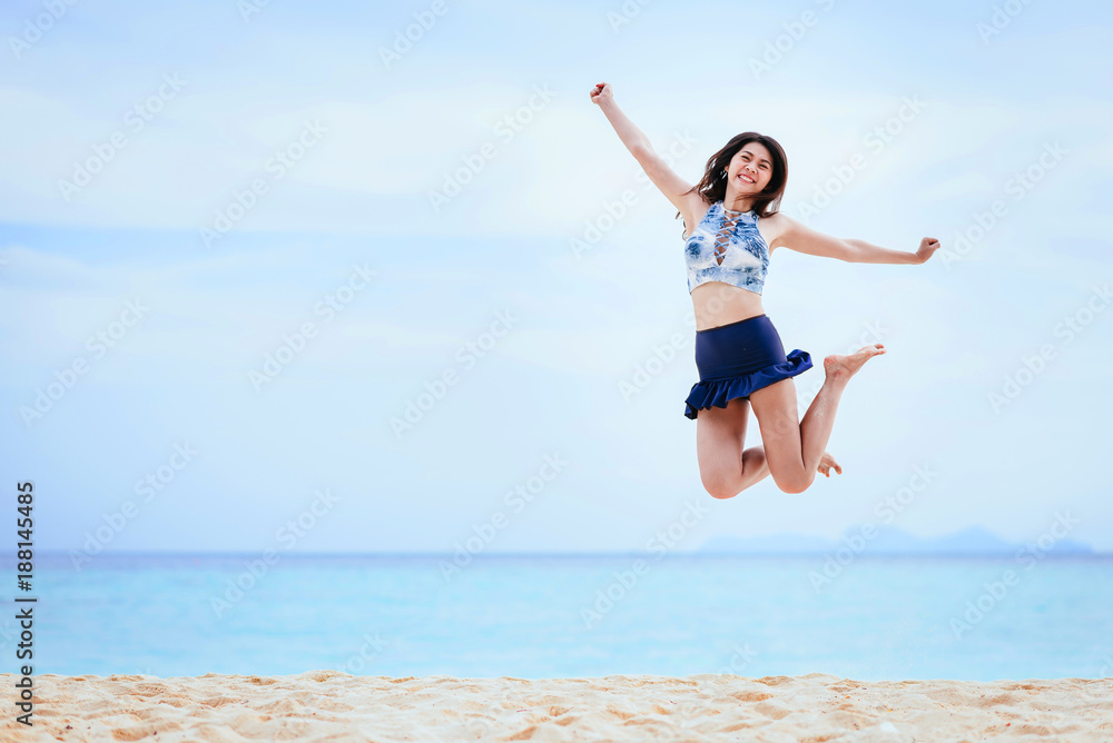 Happy and cheerful young Asian woman jumping on the beach in morning