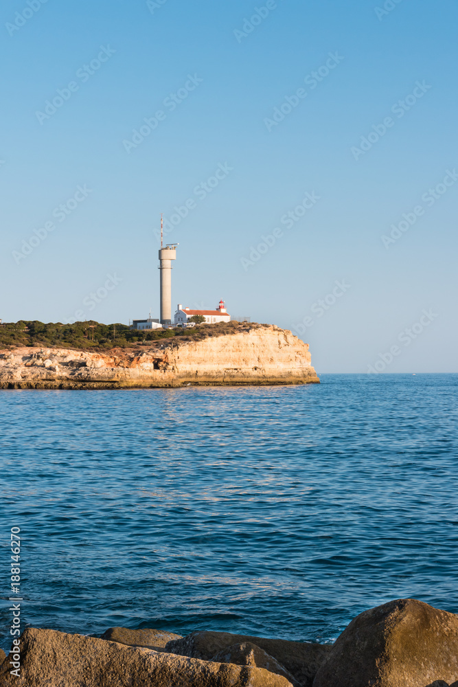 The Lighthouse of Ponta do Altar on promontory. Evening Atlantic coast view with sun reflection on water surface (Ferragudo Lagoa Algarve Portugal). The Lighthouse of Ponta do Altar on promontory. Evening Atlantic coast view with sun reflection on water surface (Ferragudo Lagoa Algarve Portugal).