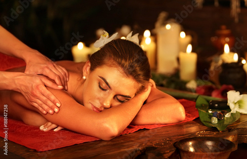 Massage of woman in spa salon. Girl on candles background treats problem back. How to spend time with health well-being. Luxary interior with working masseuse.