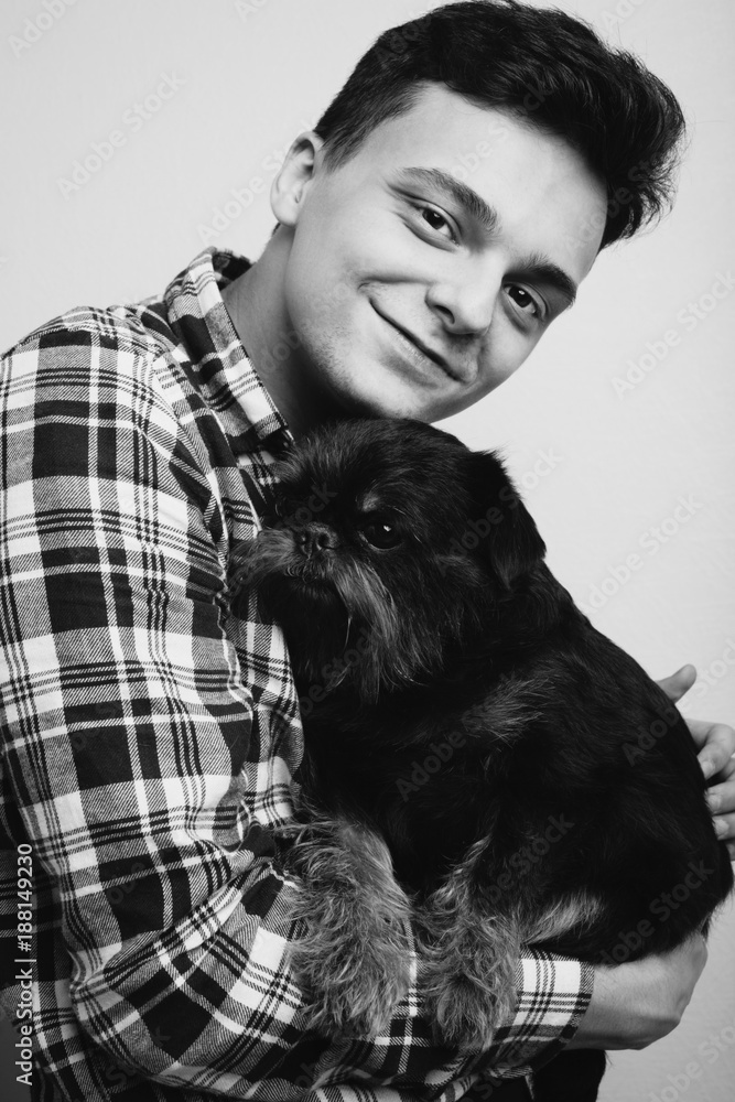 Closeup portrait handsome young hipster man, kissing his good friend black dog isolated light background. Positive human emotions, facial expression, feelings. Black and white photo Closeup portrait handsome young hipster man, kissing his good friend black dog isolated light background. Positive human emotions, facial expression, feelings. Black and white photo
