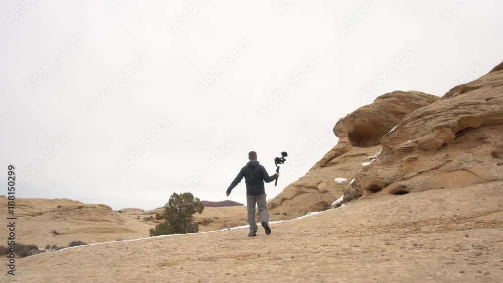 Following man running through the desert holding gimbal and camera as he records a vlog. Following man running through the desert holding gimbal and camera as he records a vlog.