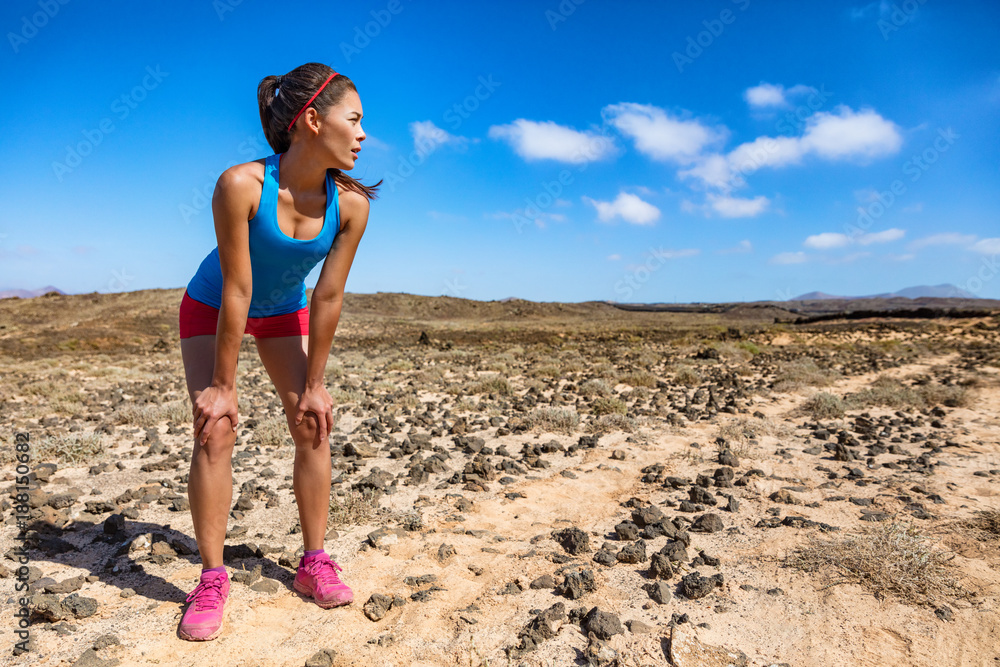 Trail runner woman tired breathing hard during ultra running cardio exercise exhausted on difficult run race. Asian young athlete in desert summer heat training hard.