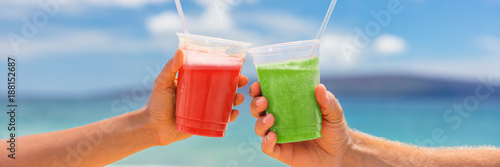 Healthy juice smoothie drinking couple toasting banner. Two fruit juices plastic cups of berry fruits or beets and green vegetable or kiwi smoothies on summer outdoors background.