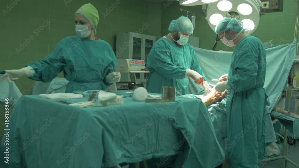 Surgeons team, nurse and anesthesiologist in protective gloves, masks and gowns using scissors,tweezers,needle and thread to sewing wound on patient knee,surgery procedure in operating room,close up. Surgeons team, nurse and anesthesiologist in protective gloves, masks and gowns using scissors,tweezers,needle and thread to sewing wound on patient knee,surgery procedure in operating room,close up.