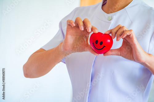 A nurse holding red heart toy. She is Left / right hand holding it.The photo shows the principle of caring and good health.