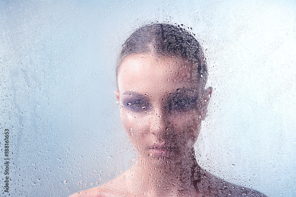 Brunette woman with makeup smoky eyes behind glass with water drops close-up