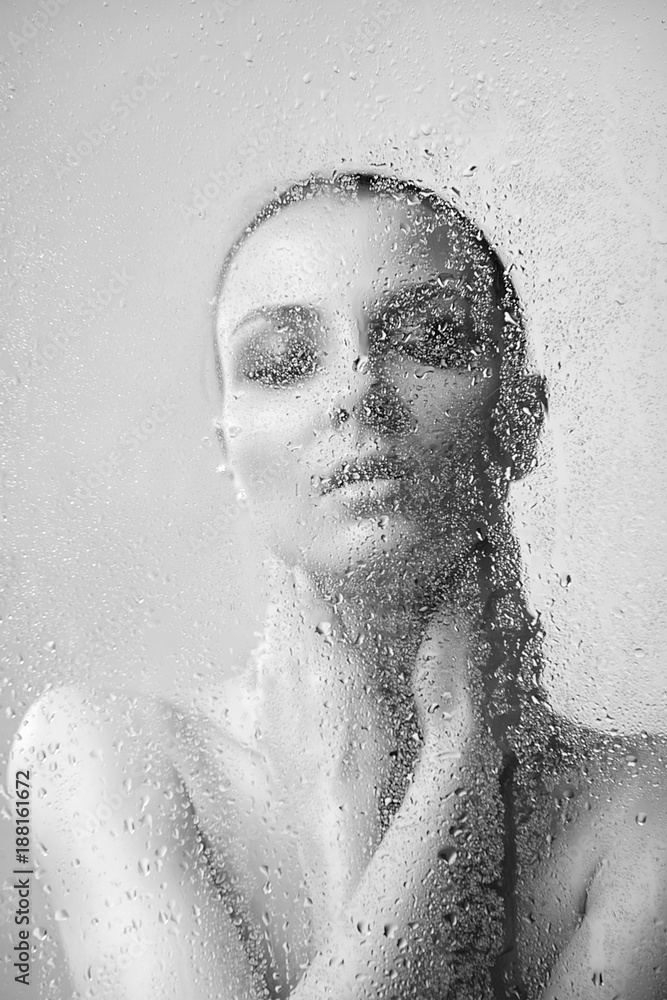 Brunette woman with makeup smoky eyes behind glass with water drops close-up black and white image
