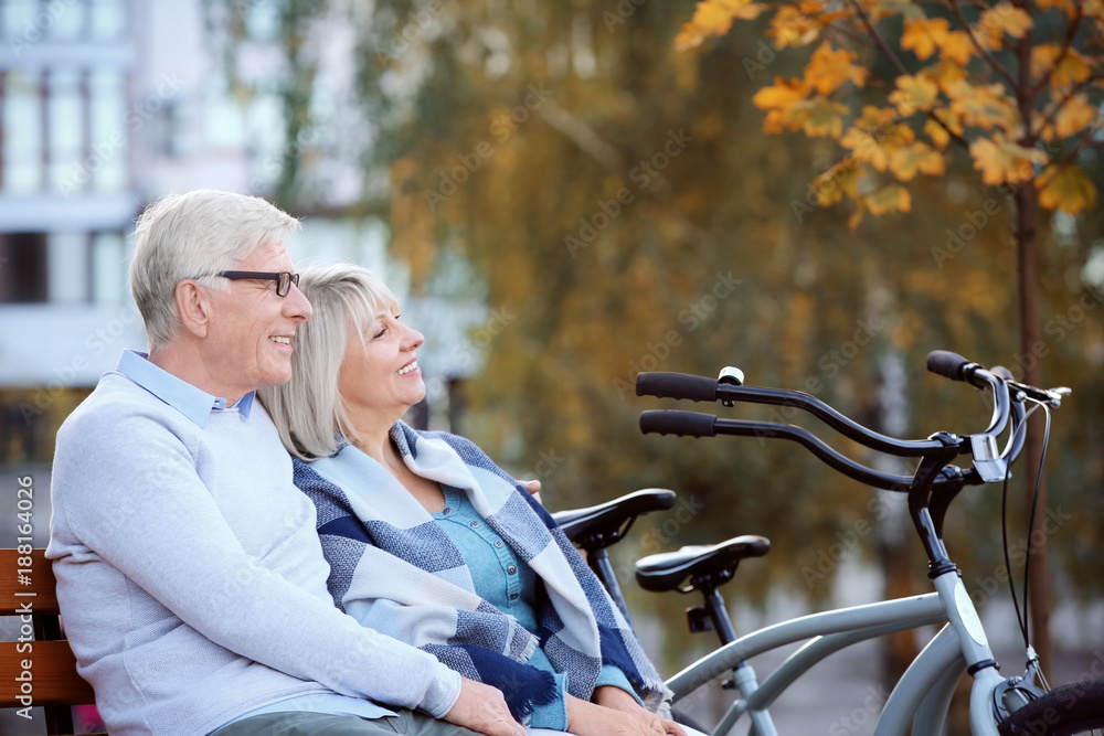 Cute elderly couple with bicycles resting in autumn park