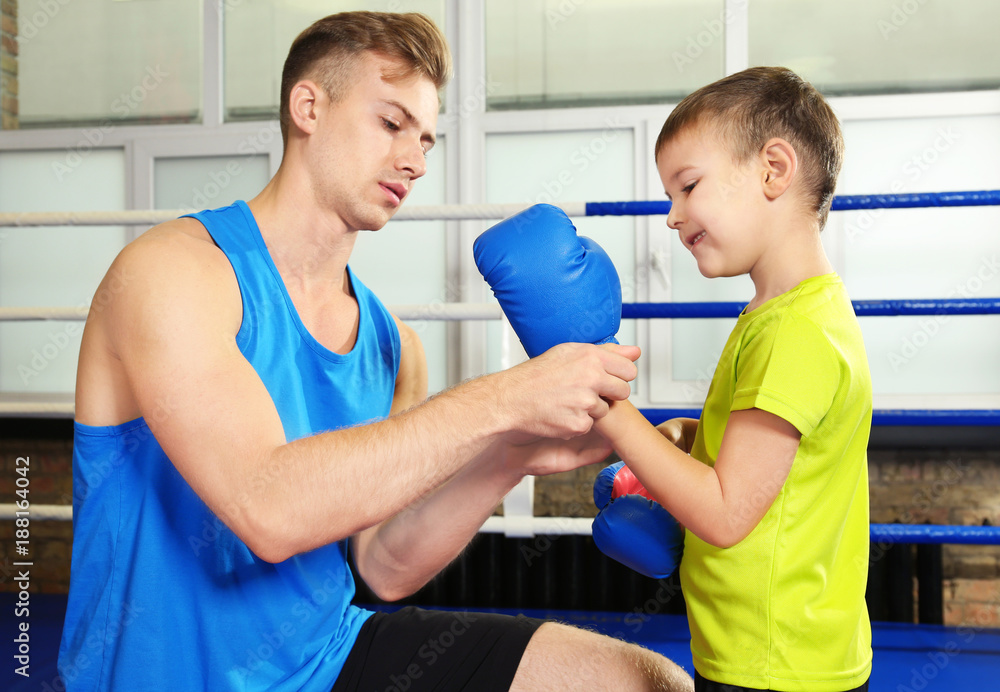 Obraz premium Trainer helping little boy put on boxing gloves in gym