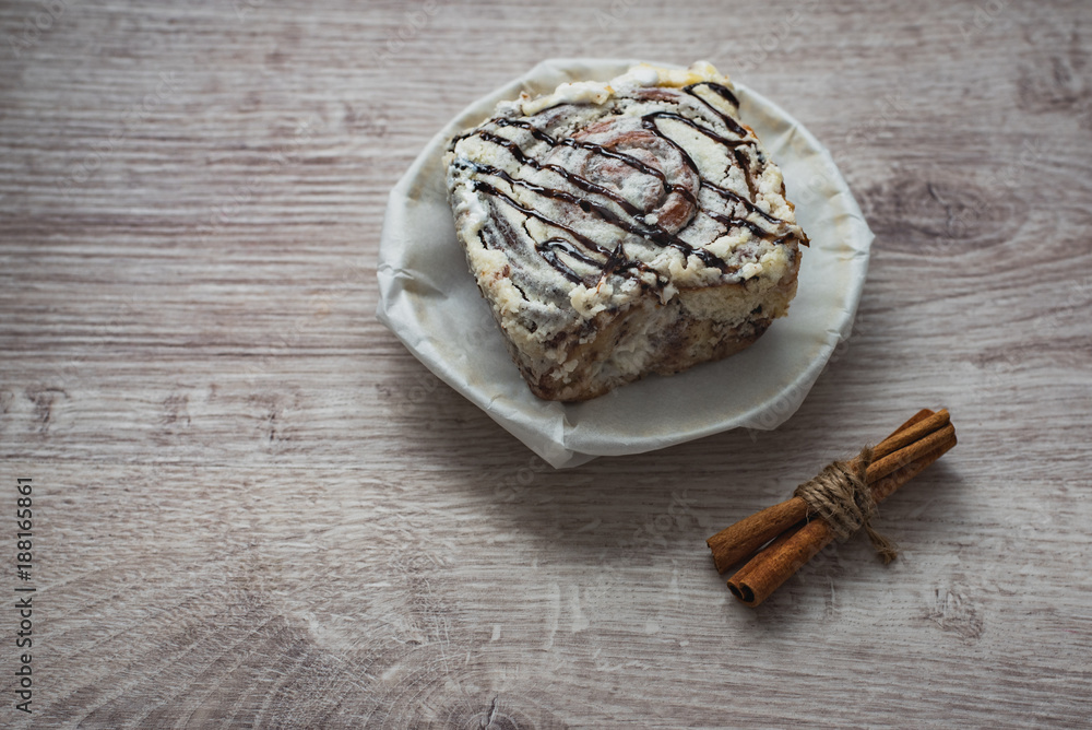 Still life of culinary spices and sweets. A sweet cake on a white porcelain plate with cinnamon sticks on a wooden surface in a cafe Still life of culinary spices and sweets. A sweet cake on a white porcelain plate with cinnamon sticks on a wooden surface in a cafe