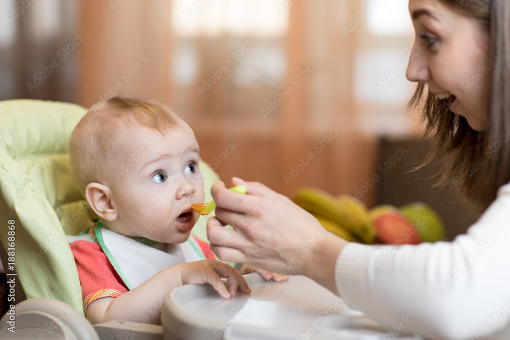 Φωτογραφία Mom giving homogenized food to her baby son on high chair.